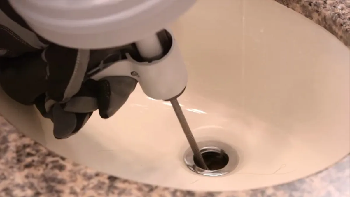 Plumber using a drain snake to clear a clogged bathroom sink drain